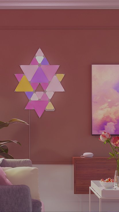 Esta es una imagen de un diseño de Nanoleaf Shapes Triangles y Mini Triangles en la pared al lado de un televisor en una sala de estar. Los paneles de luz RGB se conectan entre sí con conectores para crear un diseño.