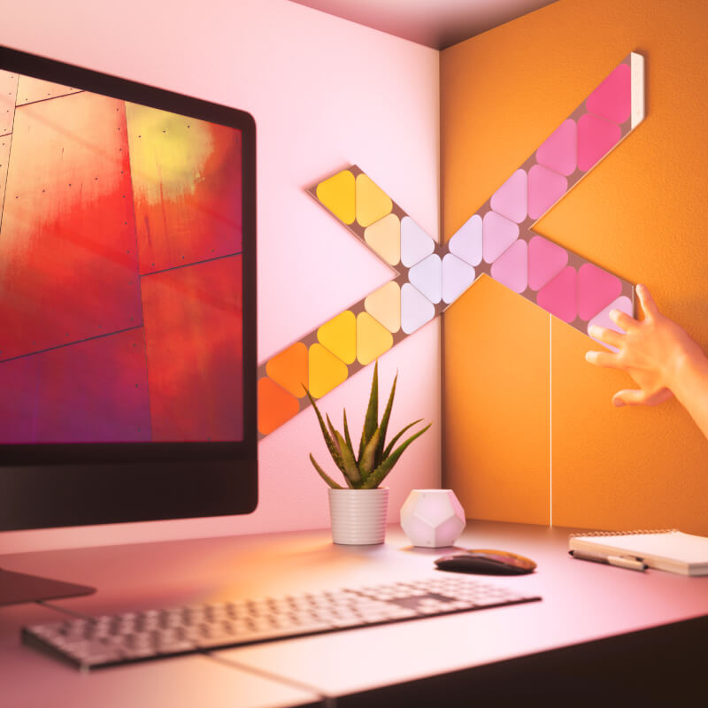 Paneles de luz inteligentes modulares con forma de minitriángulo que cambian de color y habilitados para Thread de Nanoleaf Shapes montados en una pared sobre un escritorio. Similar a Philips Hue o Lifx. HomeKit, Google Assistant, Amazon Alexa, IFTTT. 