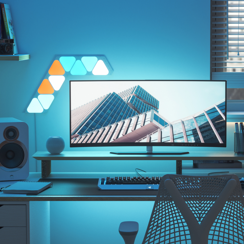 Trabalhe na configuração da mesa de casa com 9 painéis de luz minitriangulares Nanoleaf Shapes montados acima e ao redor do monitor do PC. As luzes inteligentes perfeitas para o seu escritório.